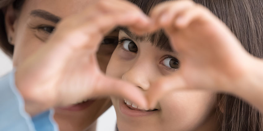 little girl smiling through hand shaped like a heart