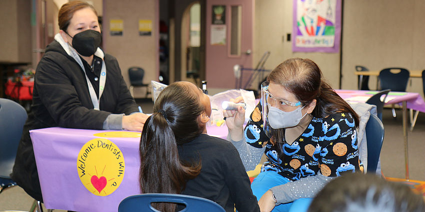 Woman looks on as dentist looks into a child's mouth