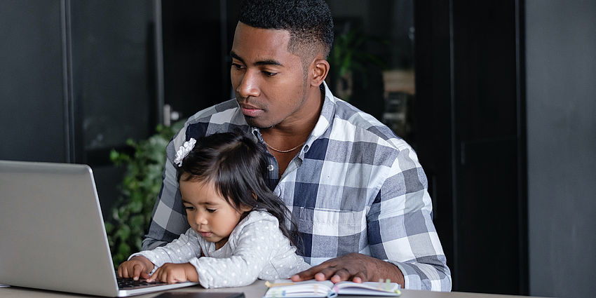 father with preschool girl on lap reaching for computer