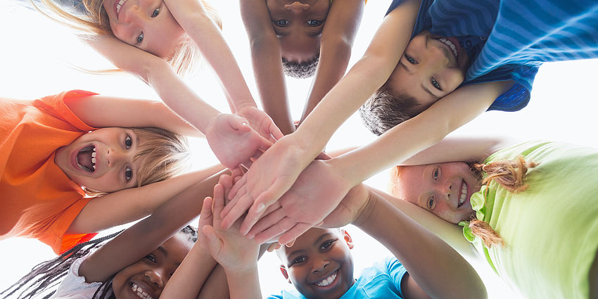 7 students looking down onto the camera with their hands in the center. 