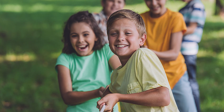 happy children playing tug of war on grassy field