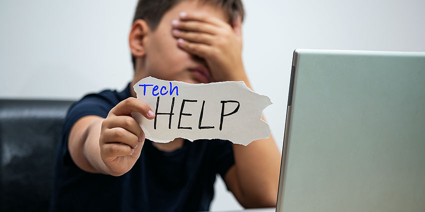 boy at laptop holding sign that says Tech Help