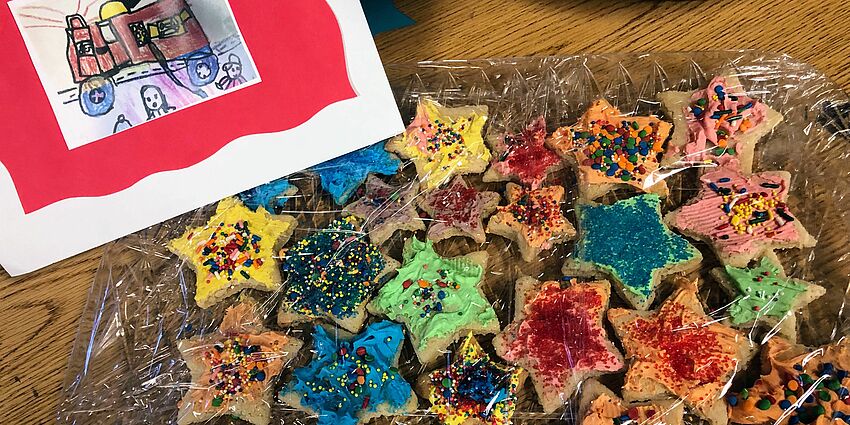 Platter of star shaped cookies with sprinkles and frosting with a drawing of a fire truck on the left hand corner. 