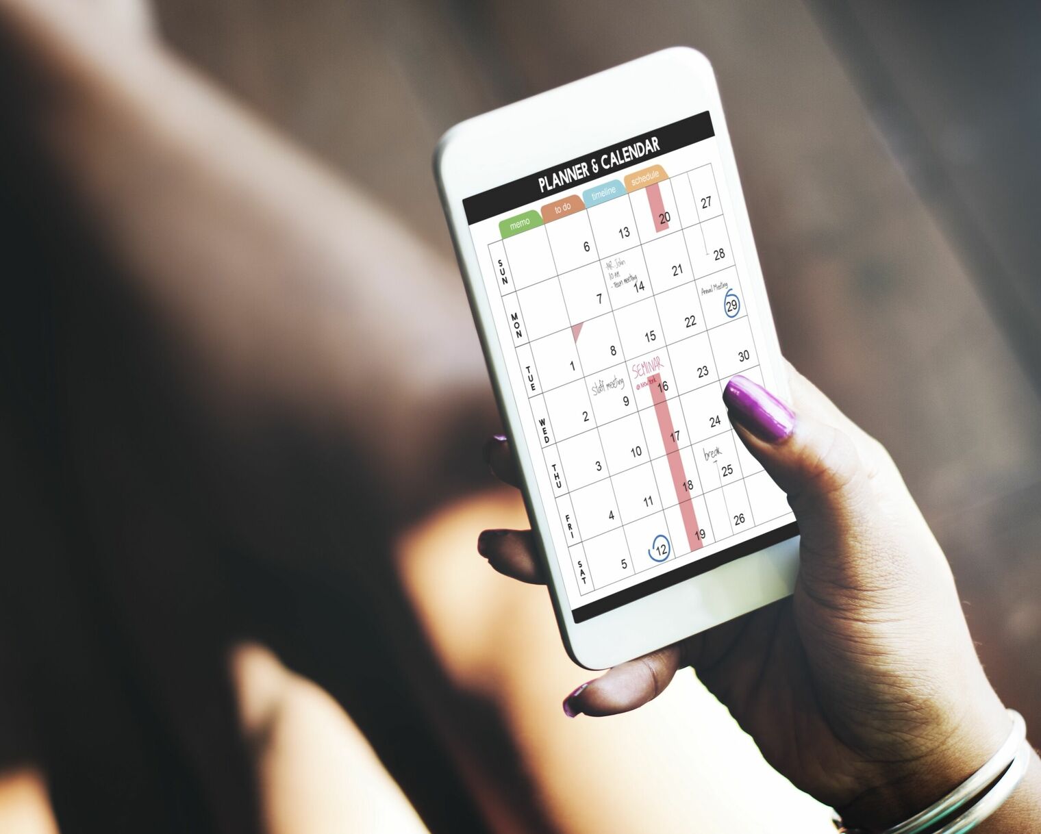 woman's hand holding a mobile device that shows a weekly planner