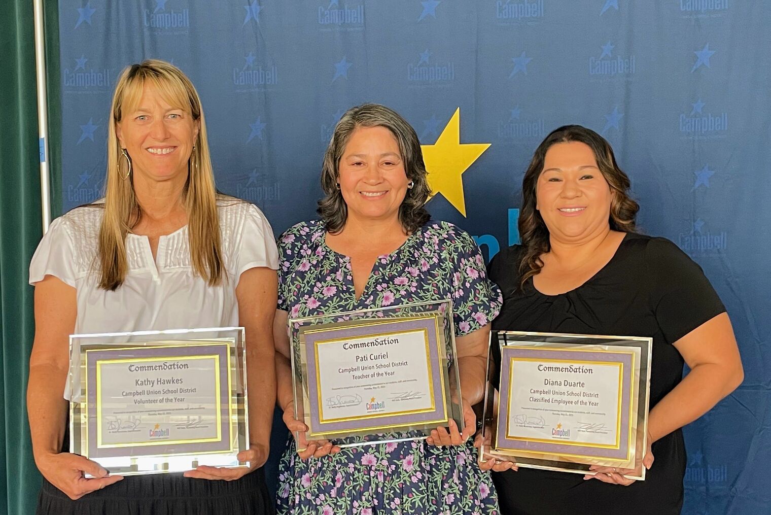 three smiling women holding framed award certificates.