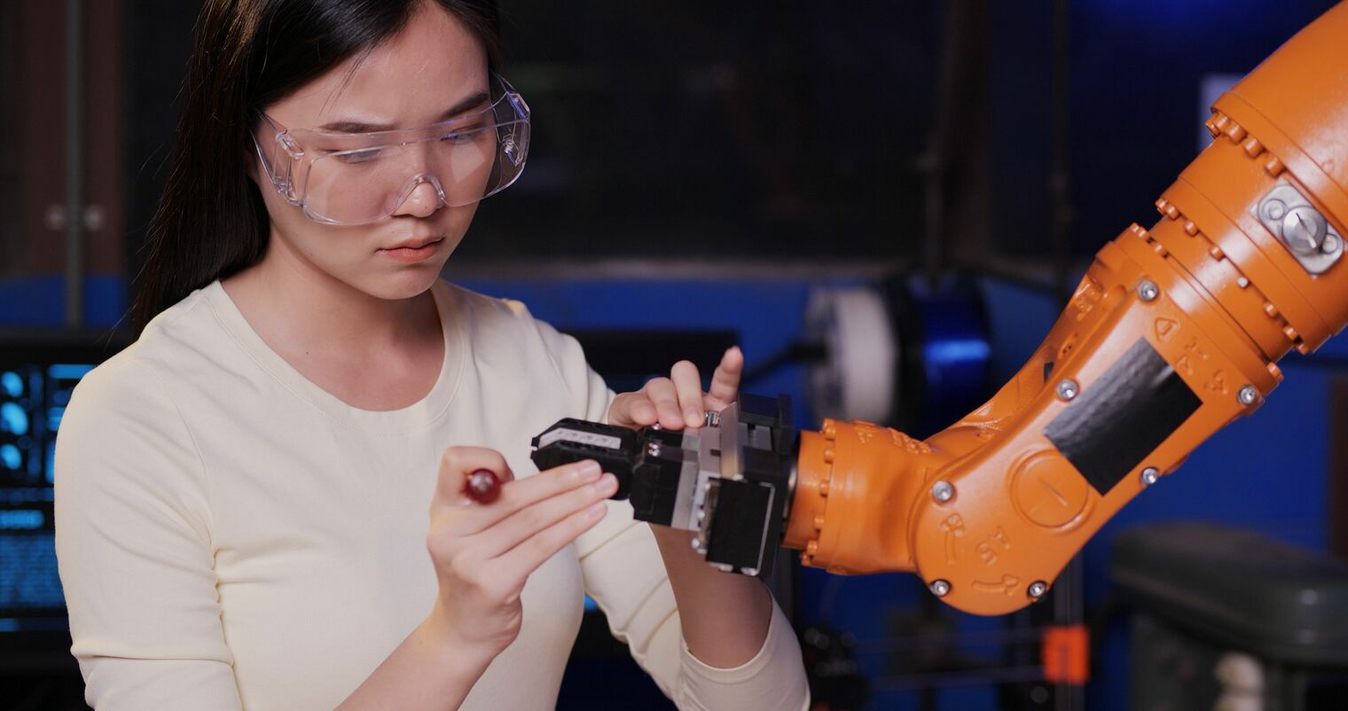 young woman wearing eye protection is fixing the end of a robotic arm