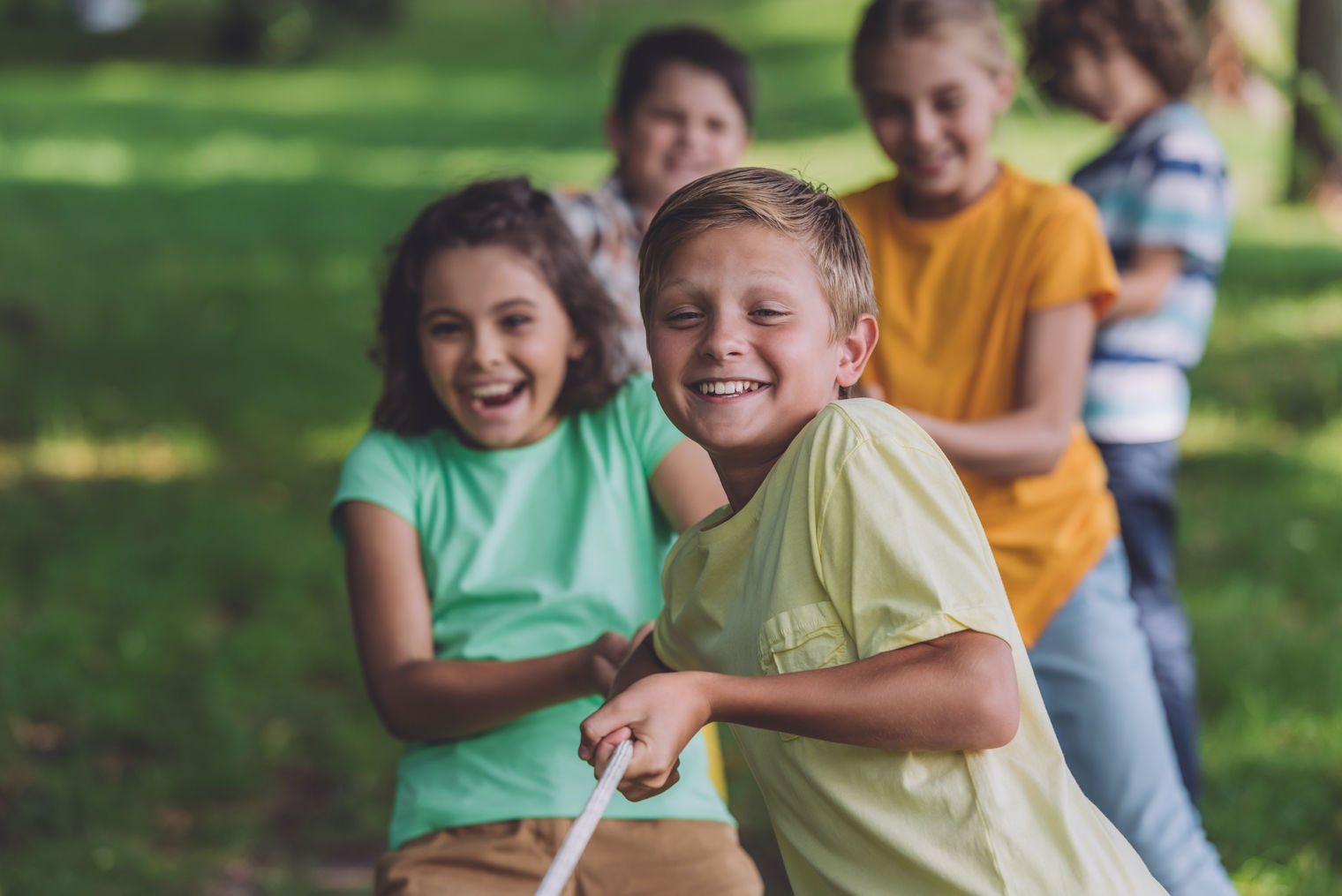 happy children playing tug of war on grassy field