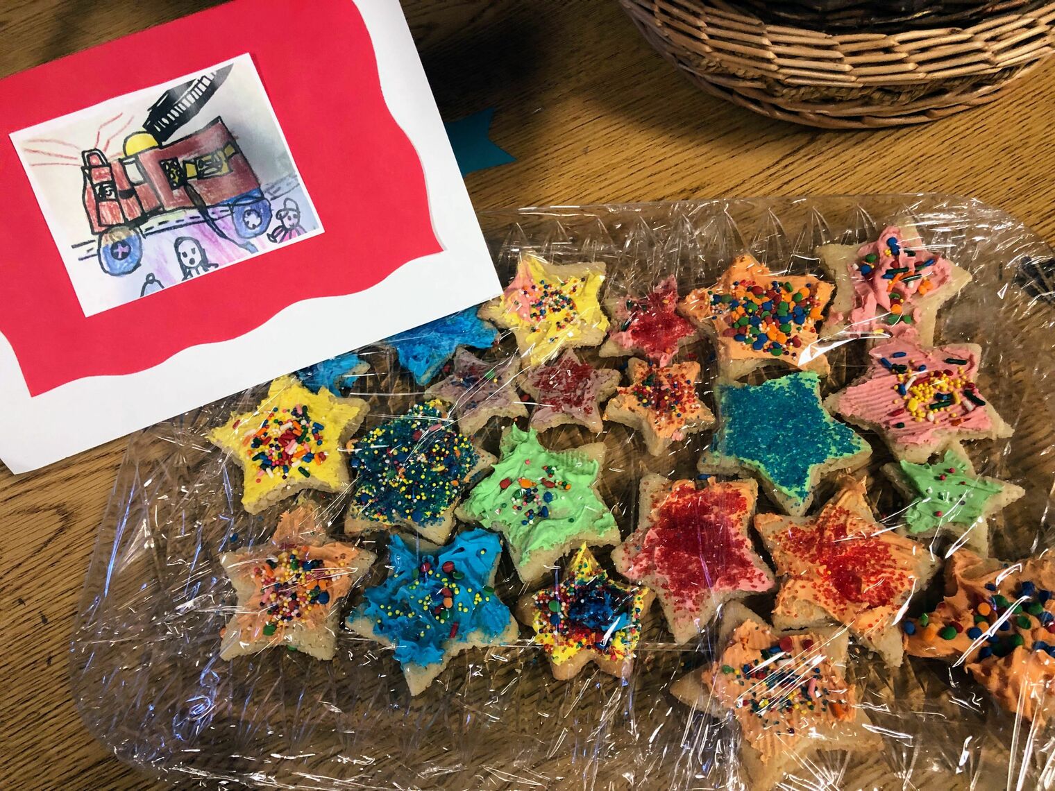 Platter of star shaped cookies with sprinkles and frosting with a drawing of a fire truck on the left hand corner. 